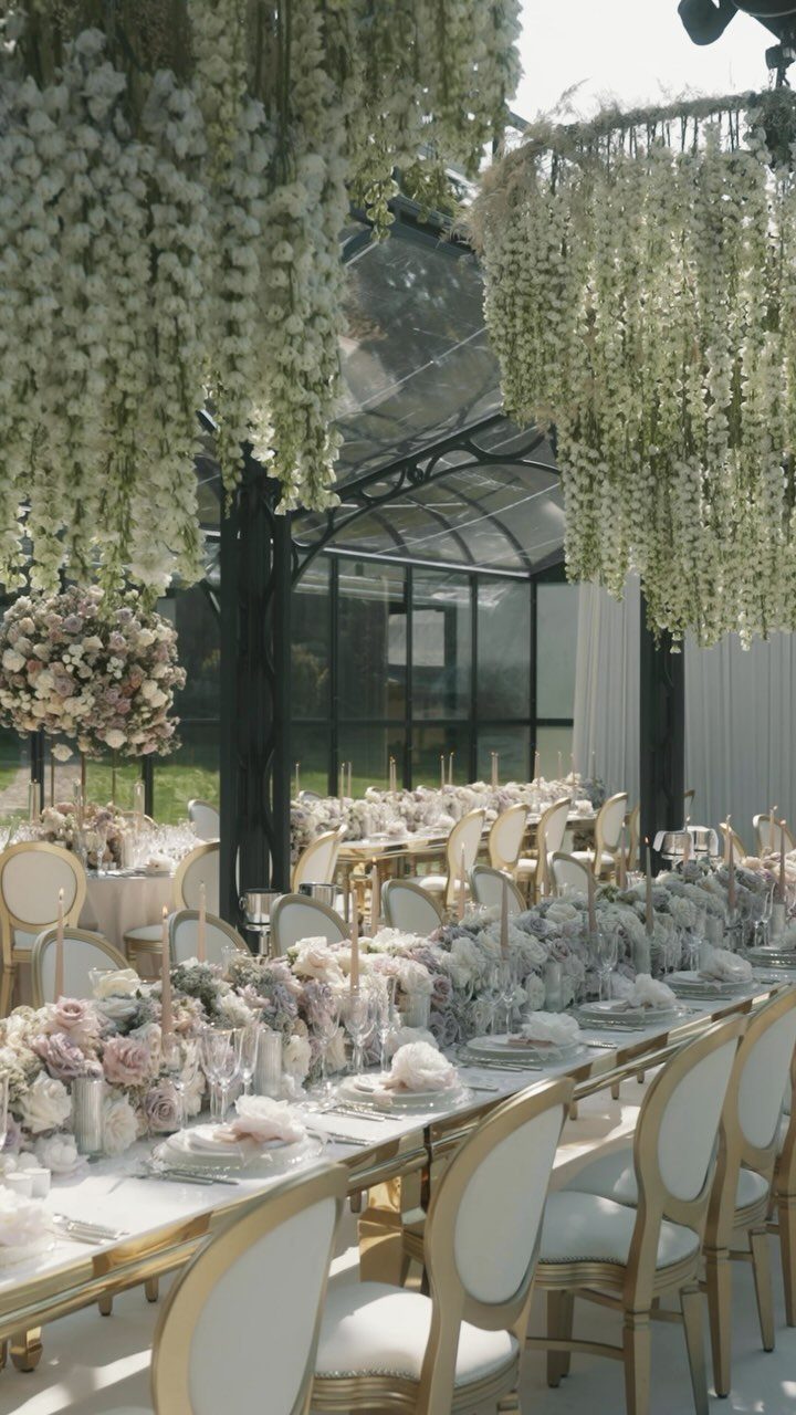 Elegant wedding table with gold chairs and hanging wisteria in a glass conservatory