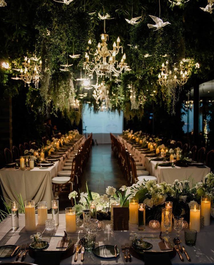 Formal dinner table with candles under a canopy of greenery and crystal chandeliers.