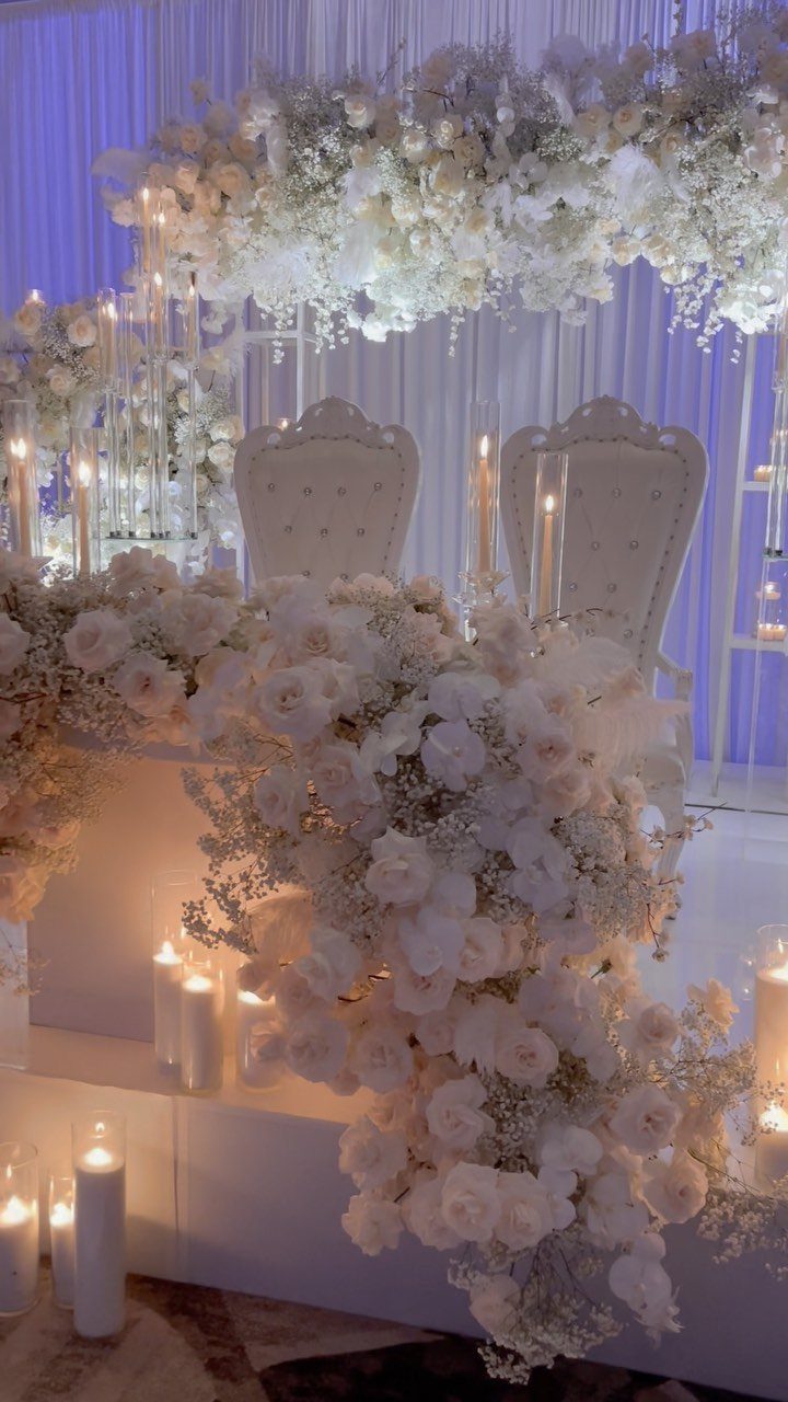 White sweetheart table decorated with cascading white roses, candles, and ornate chairs.