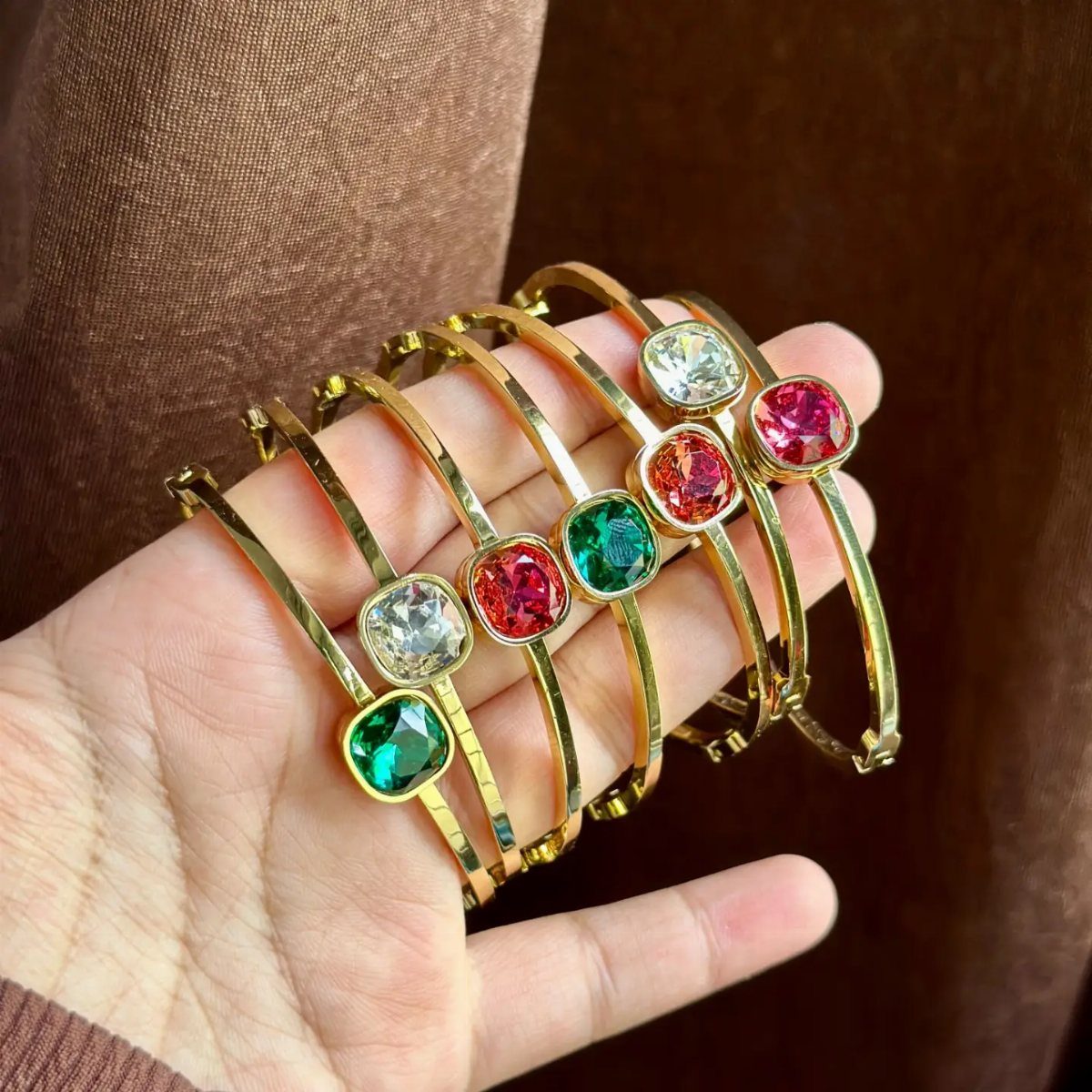 Gold bangles with large square gemstones in green, red, and clear colors.
