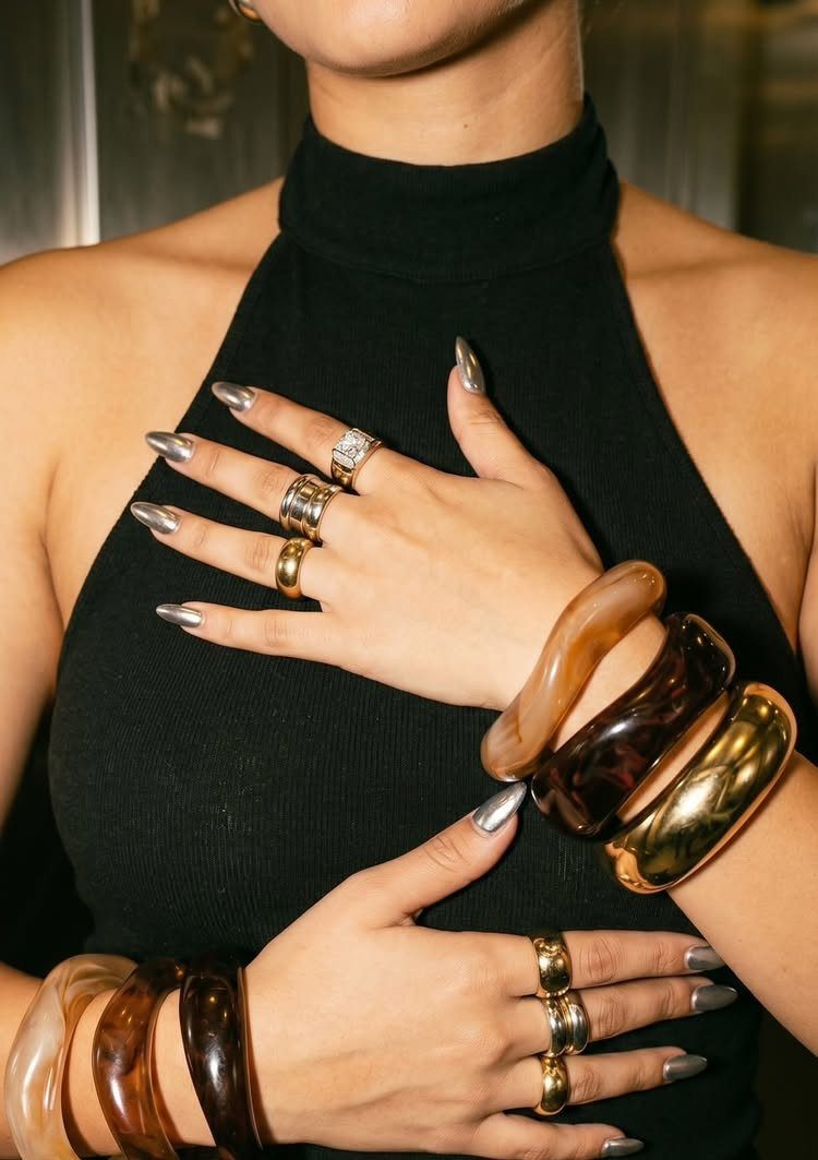 Chunky gold and amber bangles stacked on wrists with silver metallic nails.