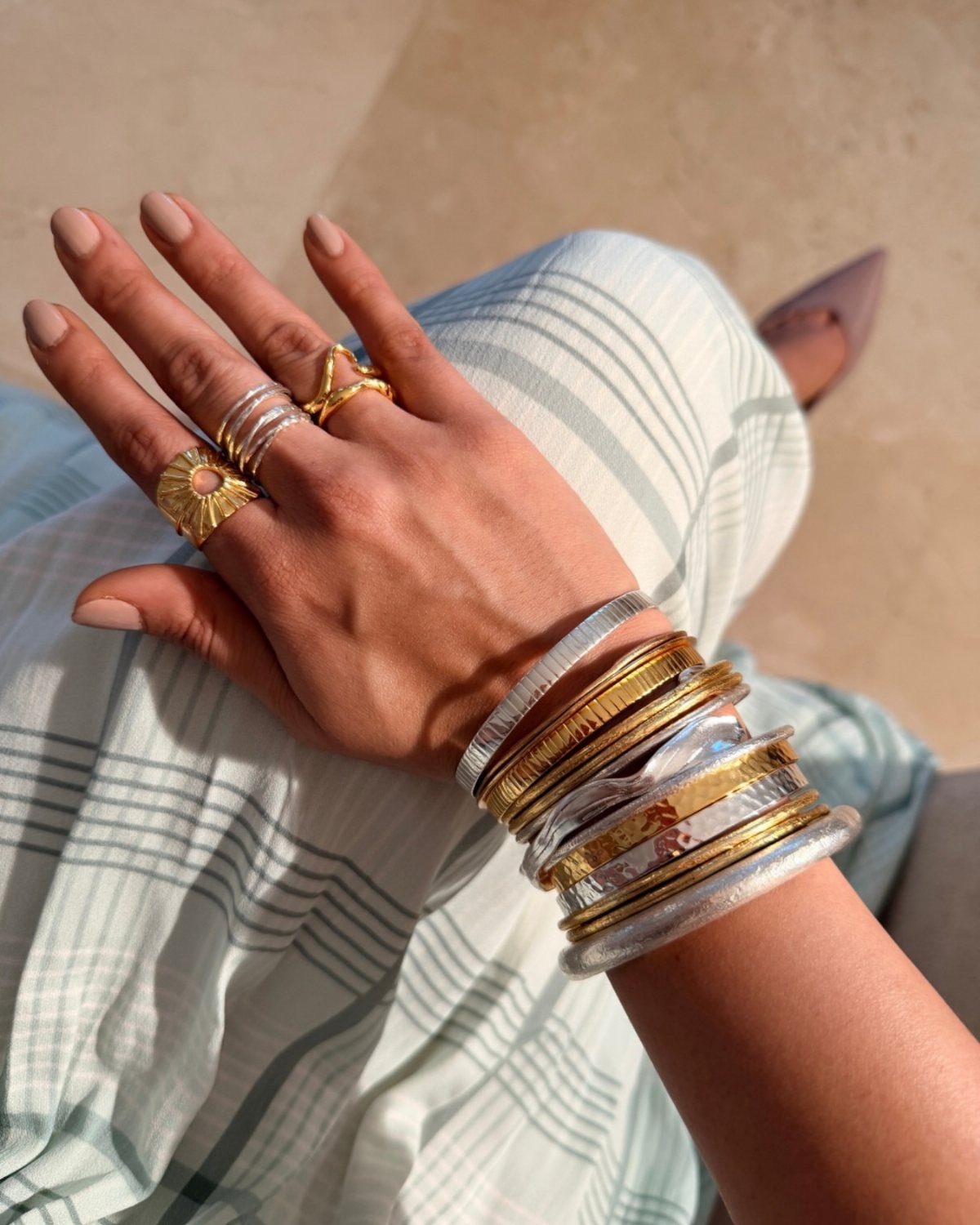 Gold and silver bangles stacked on a wrist with matching gold rings.