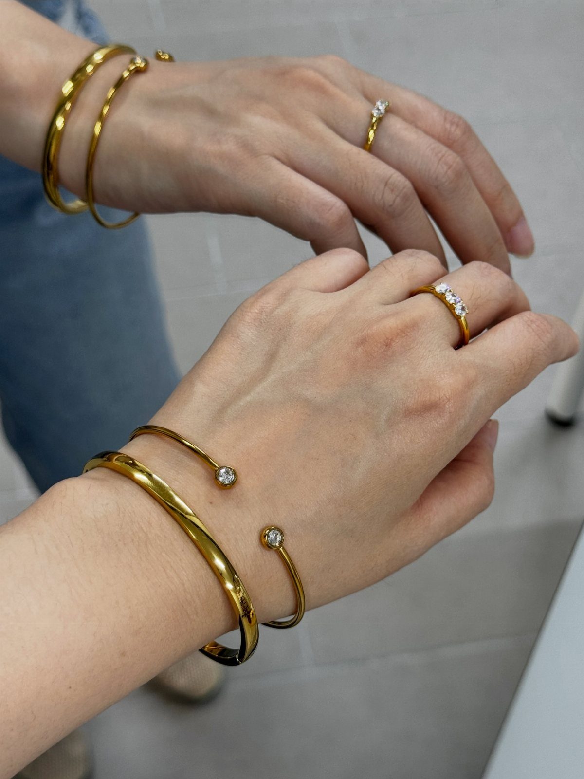 Gold bangle stacks and diamond rings worn on a person's wrists and fingers.