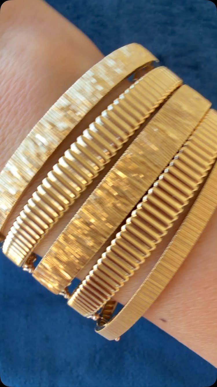 Stack of wide gold bangles with ribbed and hammered textures on a wrist.