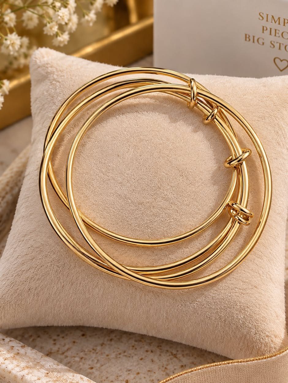 Gold bangles stacked together resting on a soft beige velvet cushion