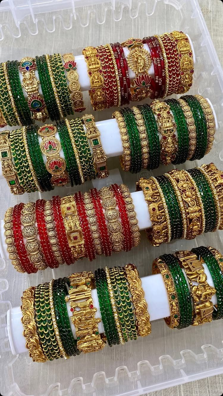 Gold-toned Indian bangles with red and green gemstones on white display holders.