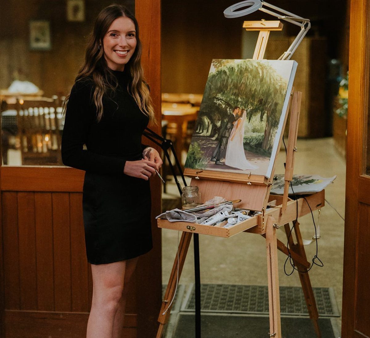 Artist standing next to a wooden easel with a wedding painting in progress.
