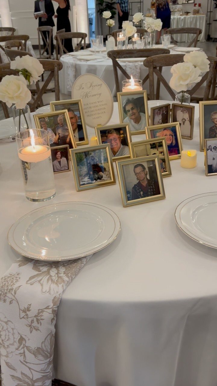Memory table with framed photographs, white roses, and lit candles on white tablecloth.