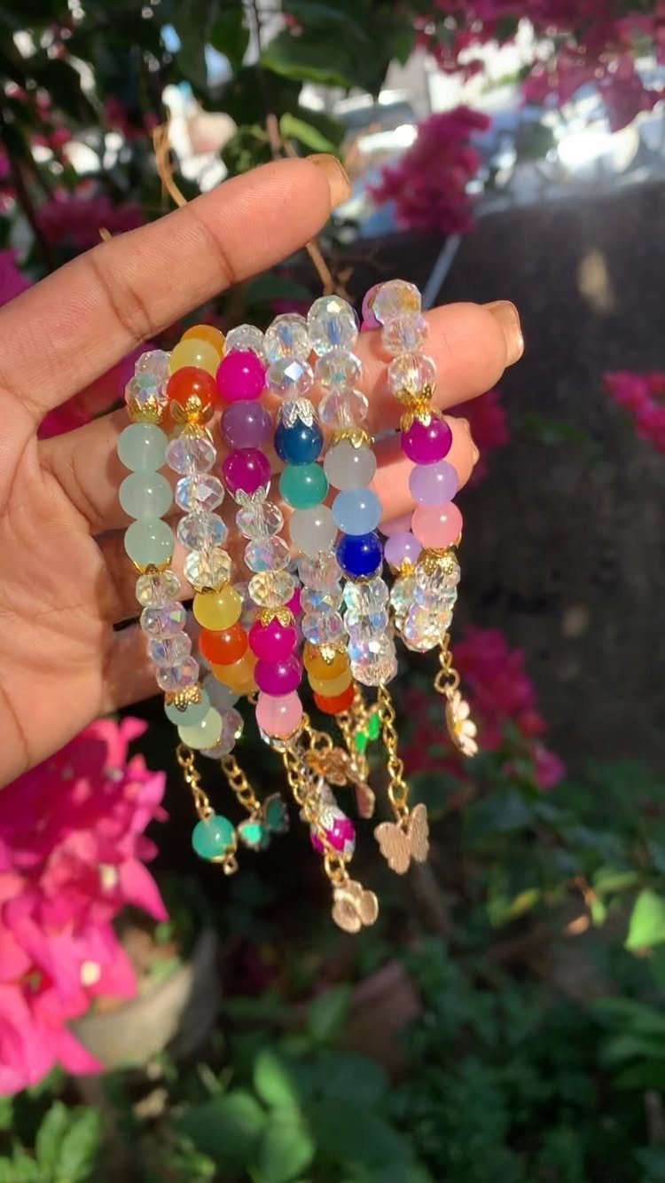 Colorful glass beaded bracelets with gold butterfly charms held against pink flowers.