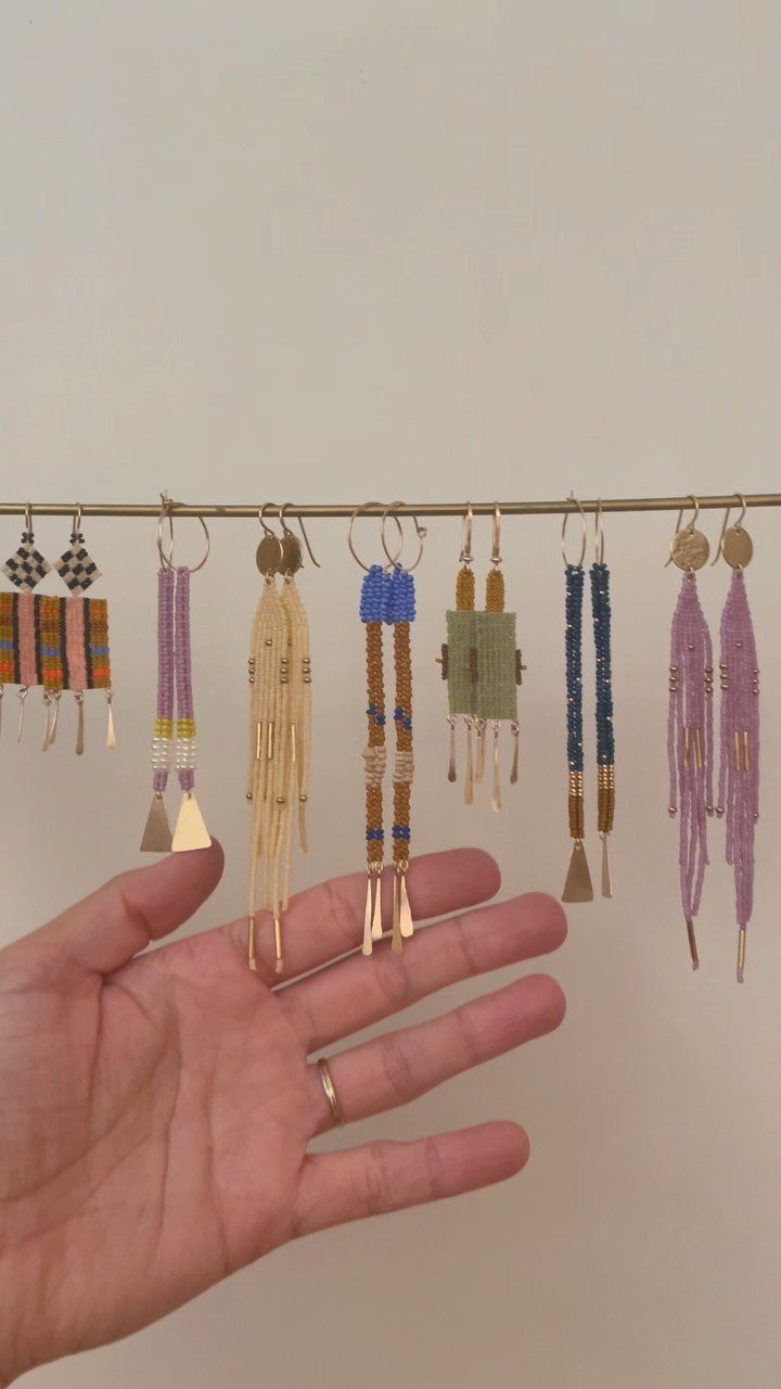 Handmade beaded earrings in various colors hanging from a gold metal bar.