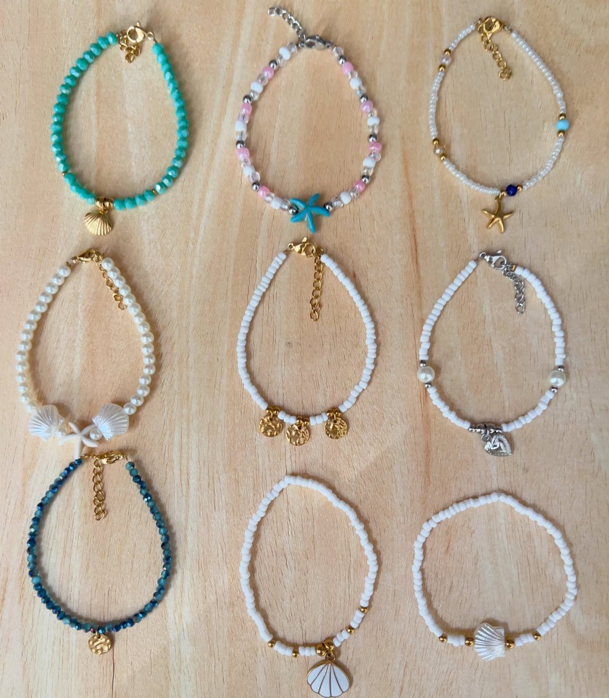 Nine handmade beaded bracelets with seashell charms on a light wooden background
