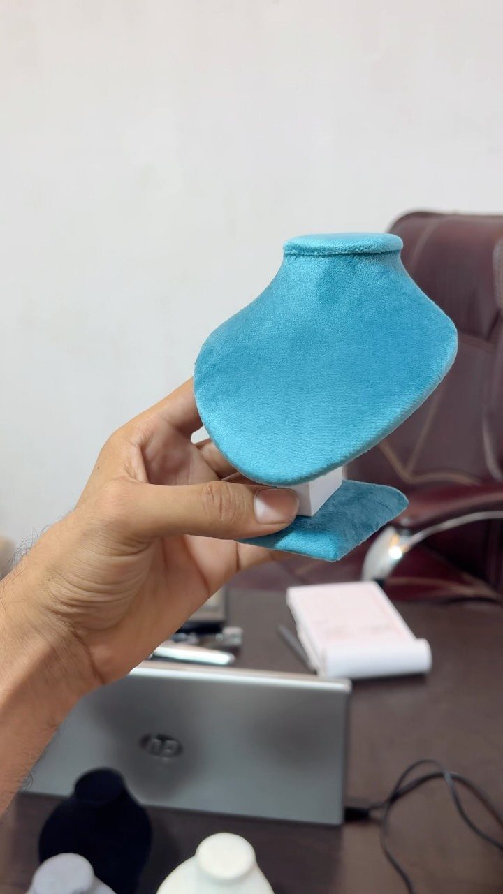 10 Jewellery Holder Ideas for Every Dressing Table 9 Turquoise velvet jewelry bust stand held by a hand over a desk.