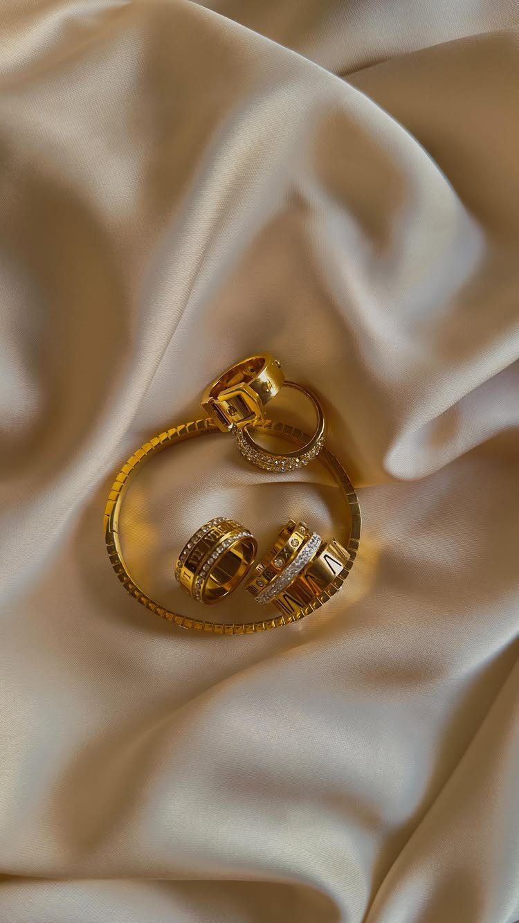 19 Jewelry Aesthetic Gold Ideas for Easy Style 19 Gold bangle, rings, and earring resting on draped cream satin fabric.