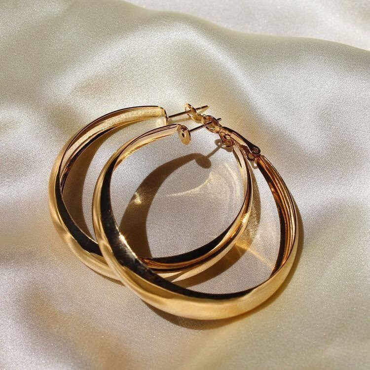 19 Jewelry Aesthetic Gold Ideas for Easy Style 12 Gold oversized hoop earrings resting on a draped cream satin fabric background.