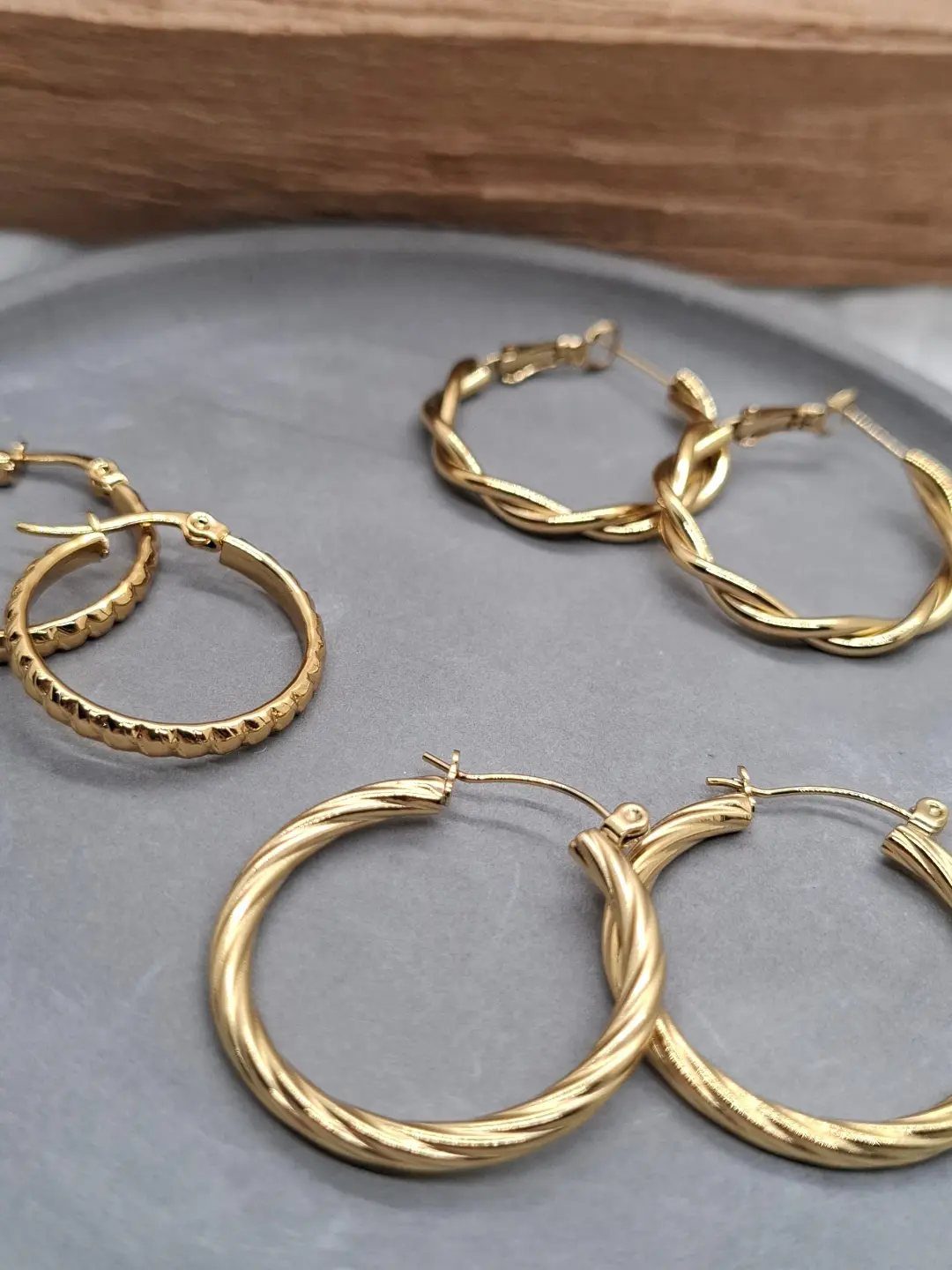 19 Jewelry Aesthetic Gold Ideas for Easy Style 10 Gold twisted rope hoop earrings of varying sizes on a grey surface.