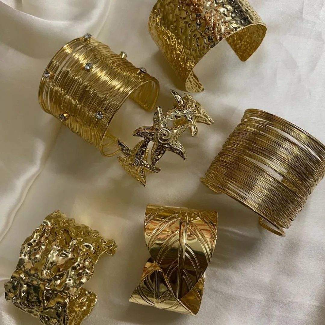 19 Jewelry Aesthetic Gold Ideas for Easy Style 3 Six wide gold cuff bracelets with different textures on white draped fabric.