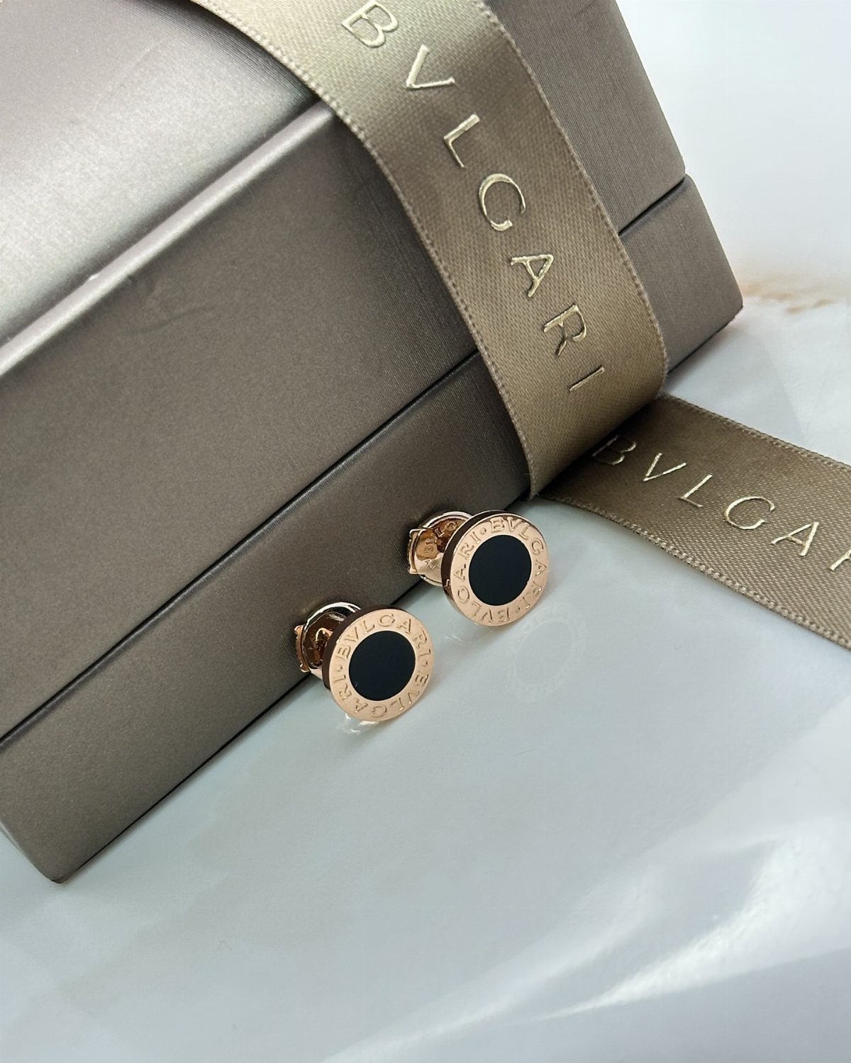 9 Jewelry Brand Logos From Tiffany Blue to Swarovski Swan 7 Gold Bvlgari stud earrings with black centers next to a branded jewelry box