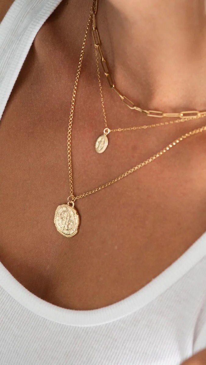 Three layered gold necklaces with pendants worn on a person in white clothing.