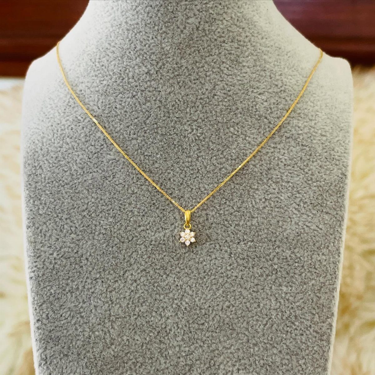 Gold chain necklace with a small flower diamond pendant on a grey bust.