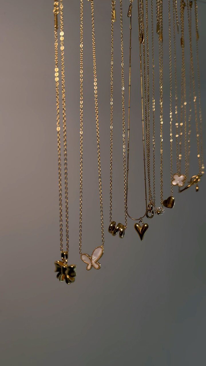 19 Jewelry Posting Ideas for Instagram That Build Sales 17 Gold necklaces with butterfly and heart pendants hanging against a grey background