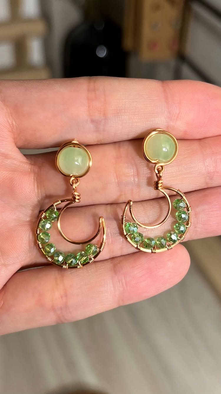 19 Jewelry Posting Ideas for Instagram That Build Sales 14 Gold crescent moon earrings with green stones held in a person's hand.