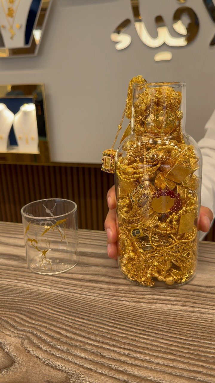 19 Jewelry Posting Ideas for Instagram That Build Sales 10 Gold jewelry pieces filling a clear glass bottle held over a wooden table.