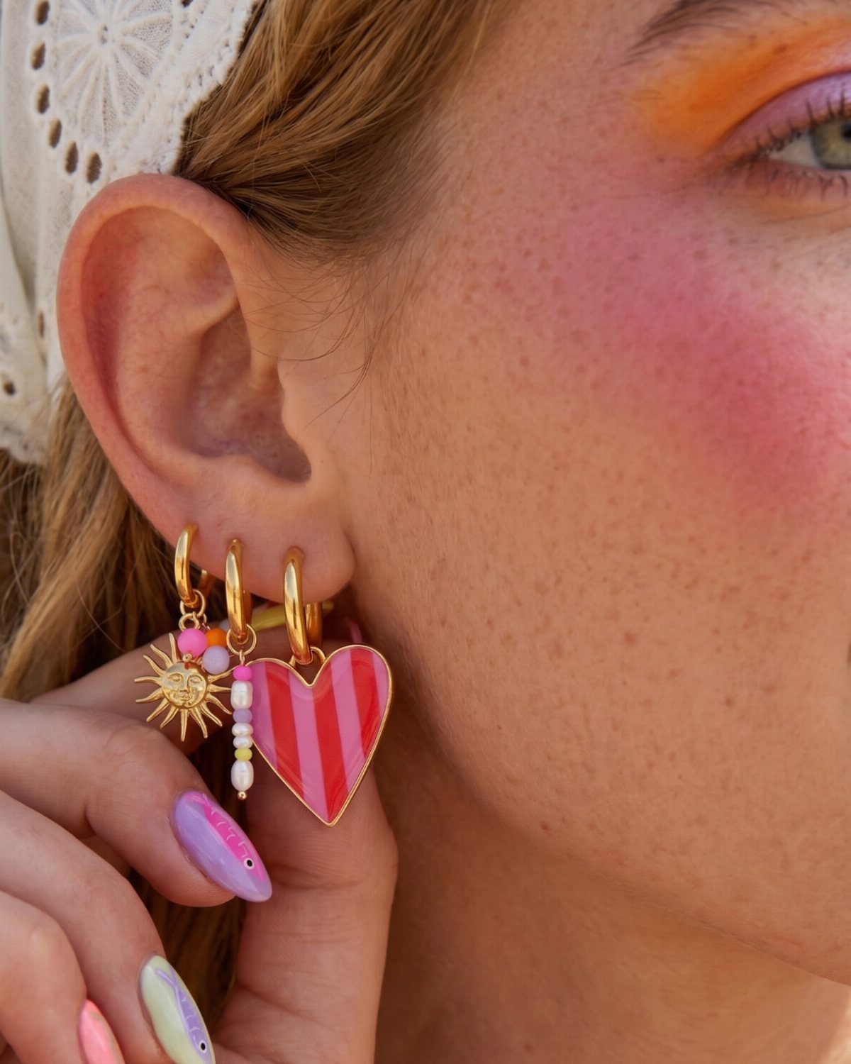 12 Jewelry Stack Inspo Earrings Ideas 7 Three gold hoop earrings with sun and heart charms on a person's ear.