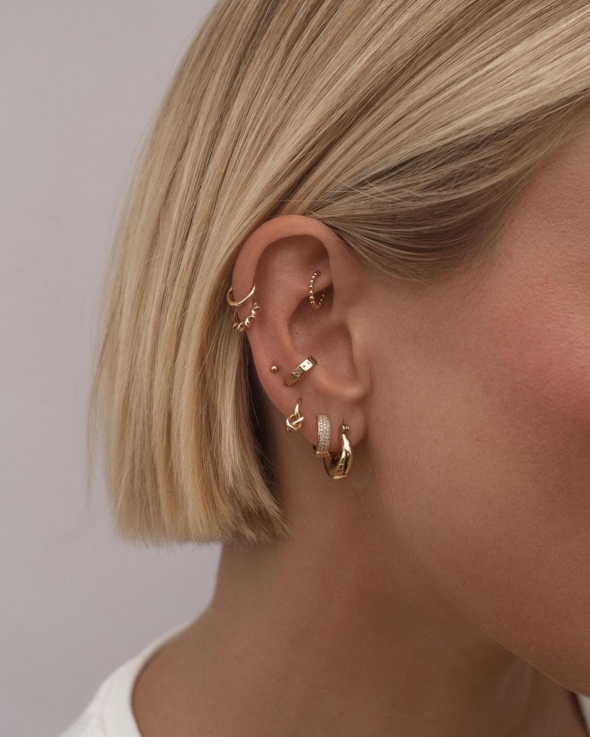 12 Jewelry Stack Inspo Earrings Ideas 1 Multiple gold hoop and stud earrings stacked on a person's ear with blonde hair.