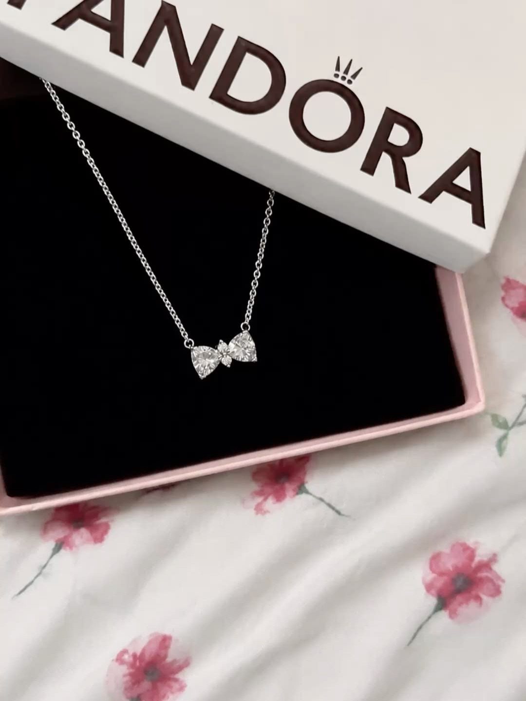 Silver bow-shaped crystal pendant necklace resting in a black Pandora jewelry box