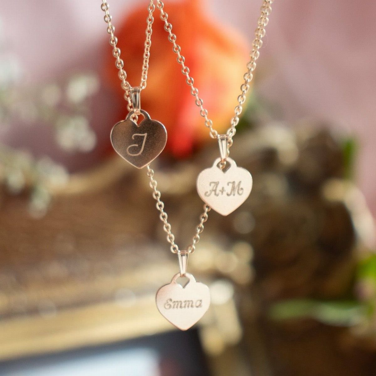 Three gold heart charm necklaces with custom engravings of a letter and names.