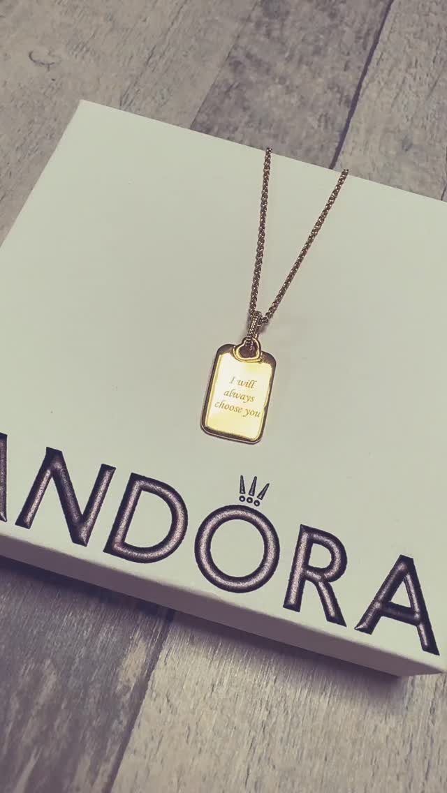 Gold chain necklace with rectangular engraved pendant on a white Pandora box