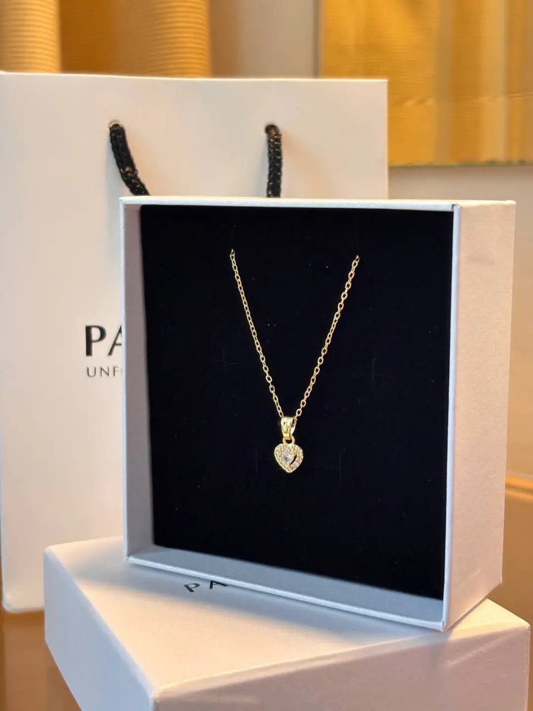 Gold heart pendant necklace displayed in a white jewelry box with a shopping bag.