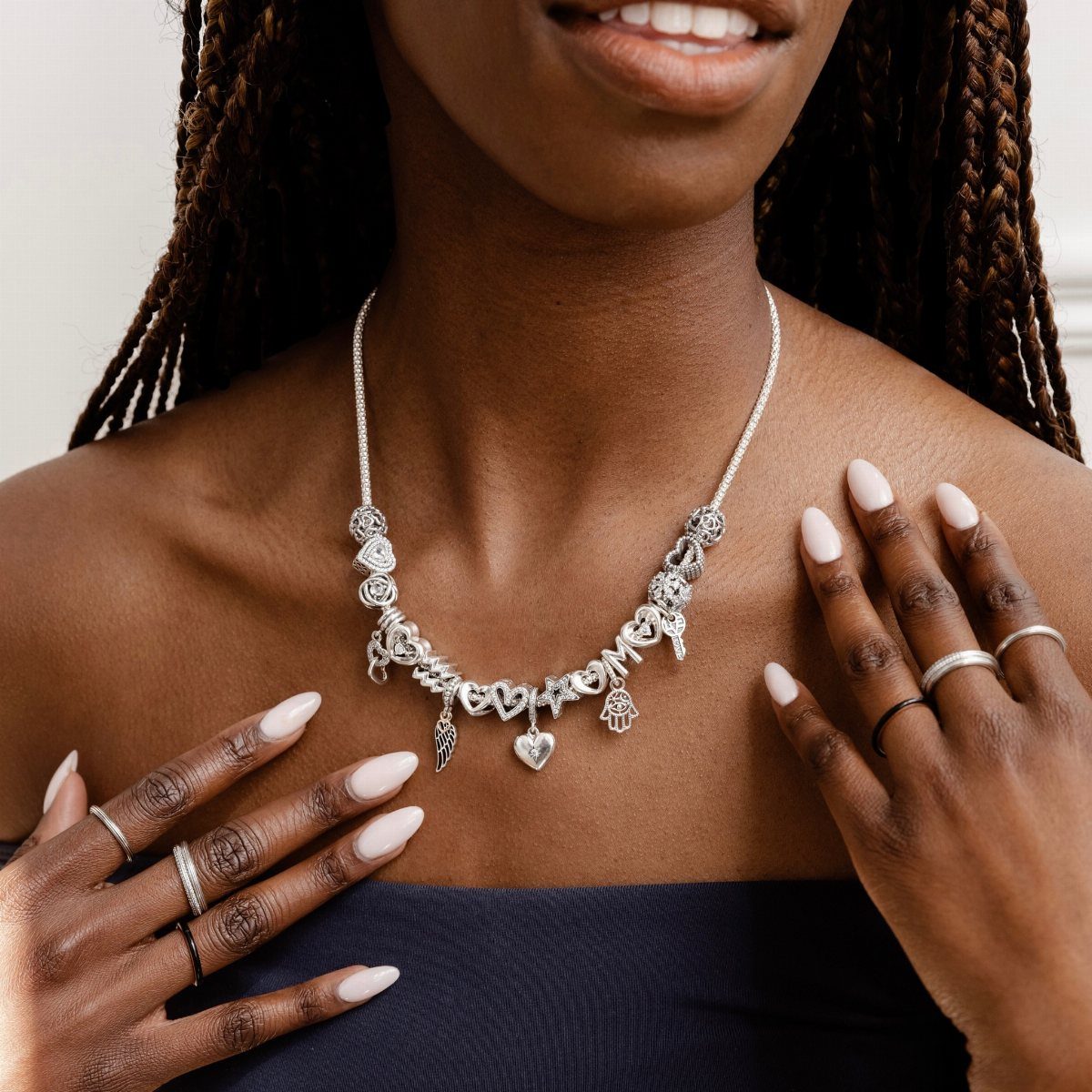 Silver charm necklace with a heart pendant worn by a person with braids