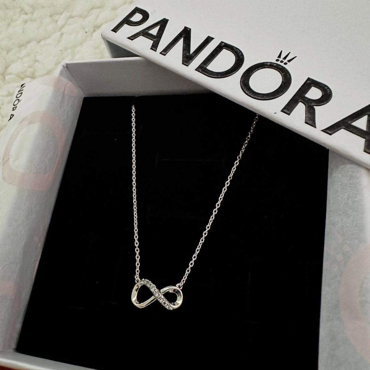 Silver infinity symbol necklace with sparkling accents inside a white Pandora jewelry box.