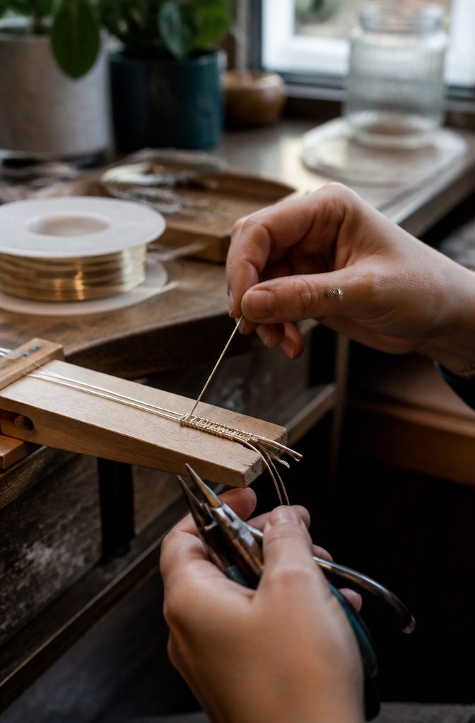 A close-up of a wire band weaving process on a bench pin.