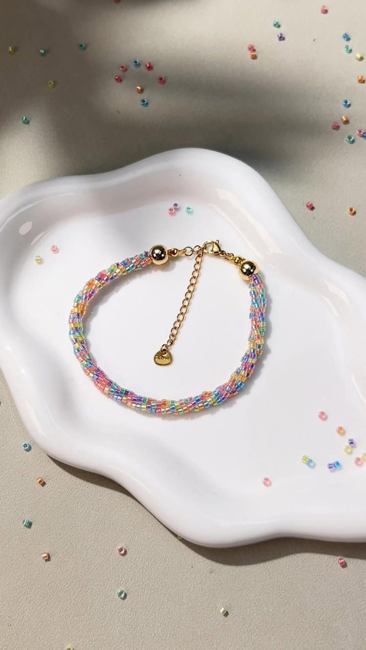 Seed Bead Crafts: 19 Patterns and Projects for 2026 13 Braided colorful seed bead bracelet on a white ceramic tray with scattered beads.