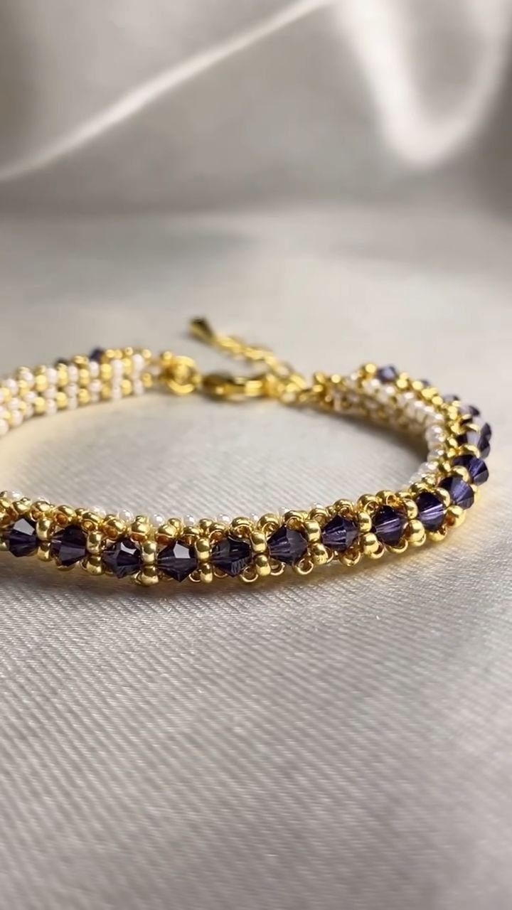 Seed Bead Crafts: 19 Patterns and Projects for 2026 1 Beaded bracelet with dark purple crystals and gold seed beads on grey fabric.
