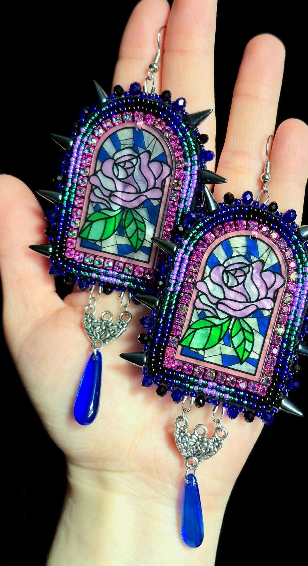Seed Bead Crafts: 19 Patterns and Projects for 2026 19 Ornate seed bead earrings with stained-glass roses and blue teardrop pendants held in hand.