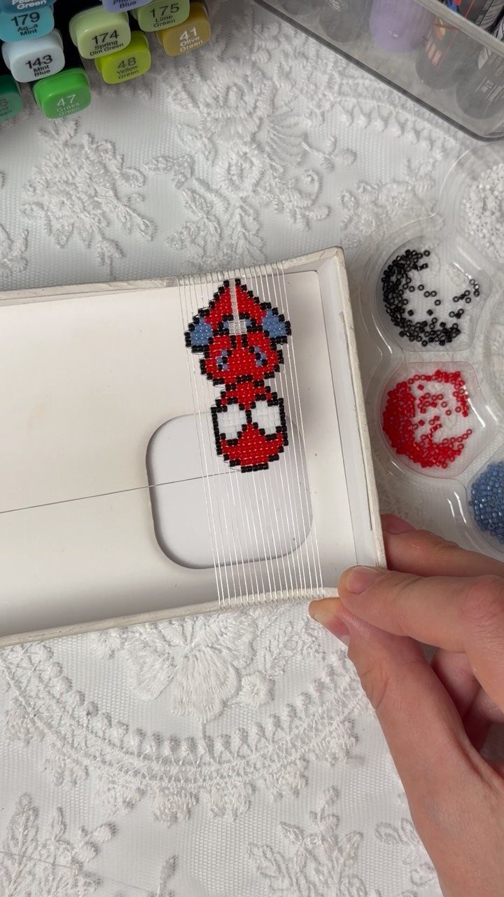 Seed Bead Crafts: 19 Patterns and Projects for 2026 12 Seed bead figure being woven on a white loom frame over lace fabric.
