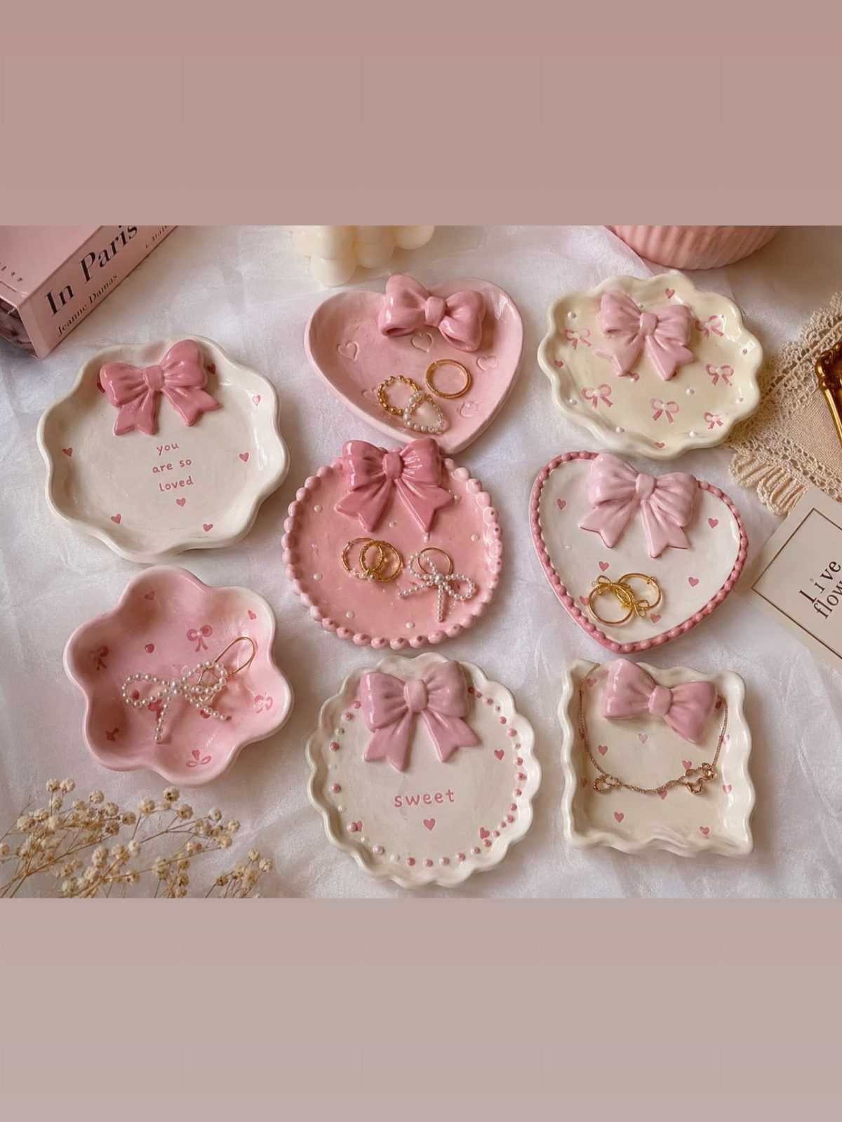 13 Stud Earring Storage Ideas for Every Jewelry Collection 8 Decorative ceramic trinket dishes with pink bows holding gold rings and earrings.
