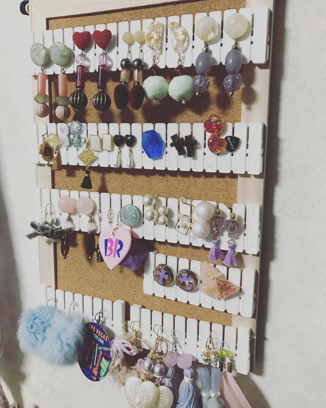 13 Stud Earring Storage Ideas for Every Jewelry Collection 2 Colorful earrings hanging from white slats on a brown cork board display.
