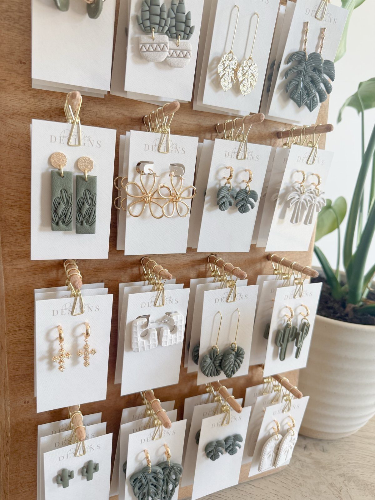 13 Stud Earring Storage Ideas for Every Jewelry Collection 9 Earrings on white cards clipped to a wooden display board with a plant.