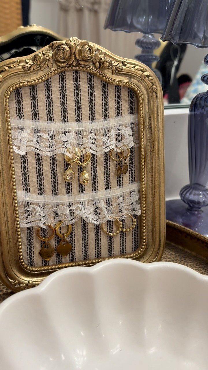13 Stud Earring Storage Ideas for Every Jewelry Collection 3 Gold ornate picture frame holding gold earrings on white lace strips.