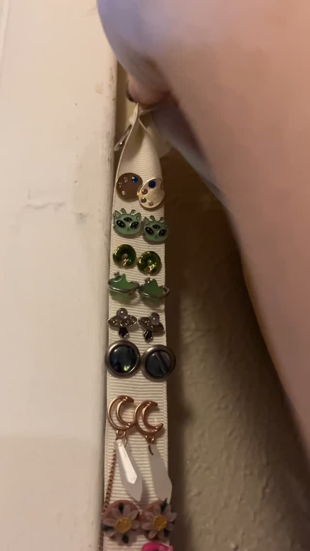 13 Stud Earring Storage Ideas for Every Jewelry Collection 11 White fabric ribbon holding various colorful stud earrings hanging against a white wall