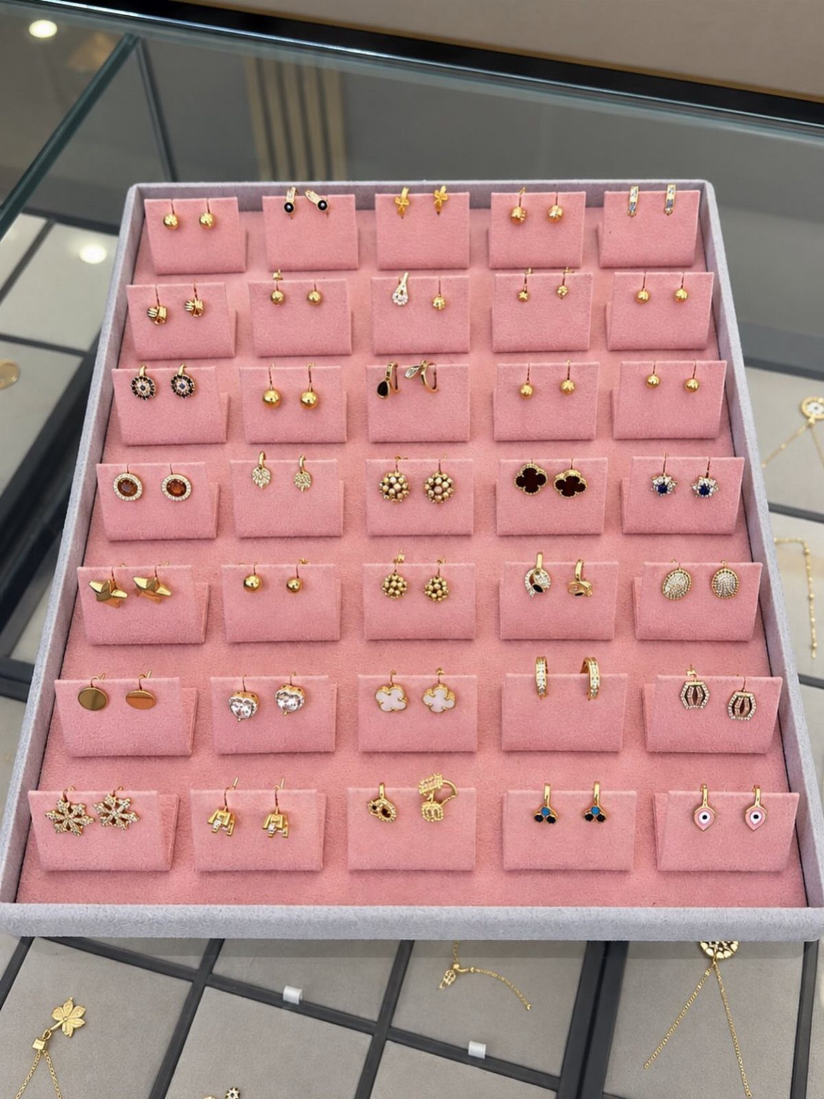 13 Stud Earring Storage Ideas for Every Jewelry Collection 7 Gold stud earrings displayed on pink velvet cushions inside a grey jewelry tray.