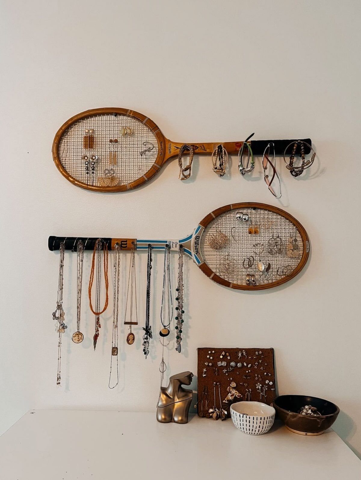13 Stud Earring Storage Ideas for Every Jewelry Collection 10 Vintage tennis rackets mounted on a wall holding various earrings and necklaces.