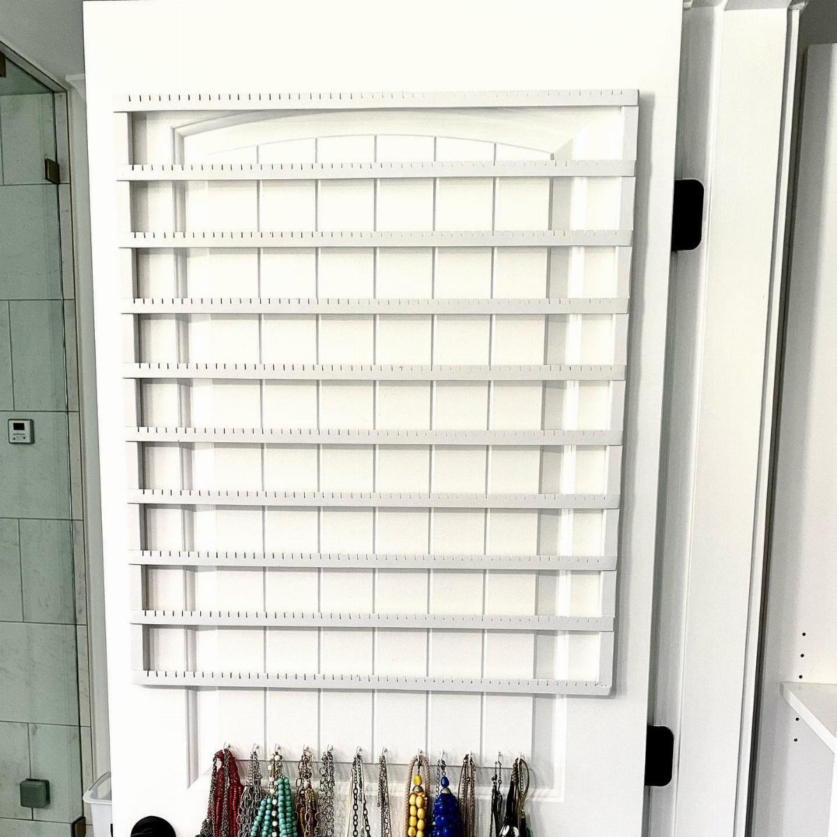 13 Stud Earring Storage Ideas for Every Jewelry Collection 13 White wall-mounted earring organizer with multiple slots and hanging beaded jewelry below.