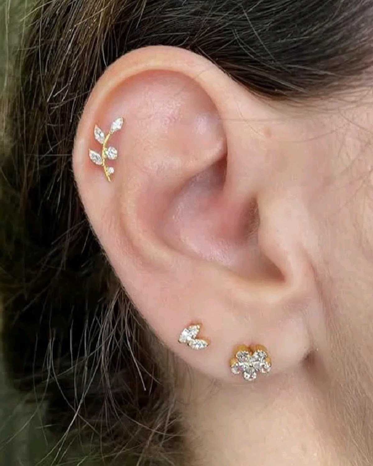 Top of the Ear Piercing Jewelry: 11 Ideas 1 Ear with gold leaf helix piercing and sparkling lobe studs against dark hair