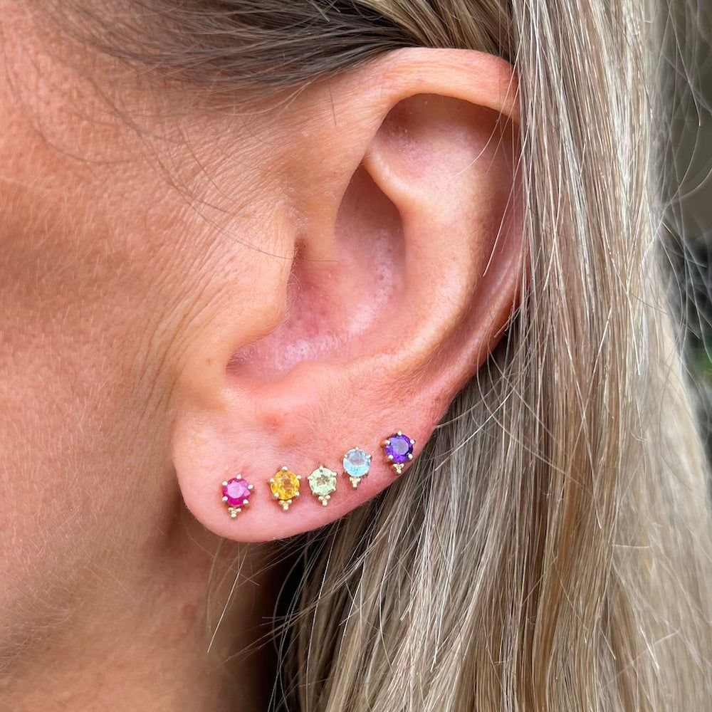 XOXO Jewelry Ideas: 10 Ways to Wear These Timeless Symbols 3 Five colorful gemstone stud earrings in gold settings arranged along a person's earlobe.