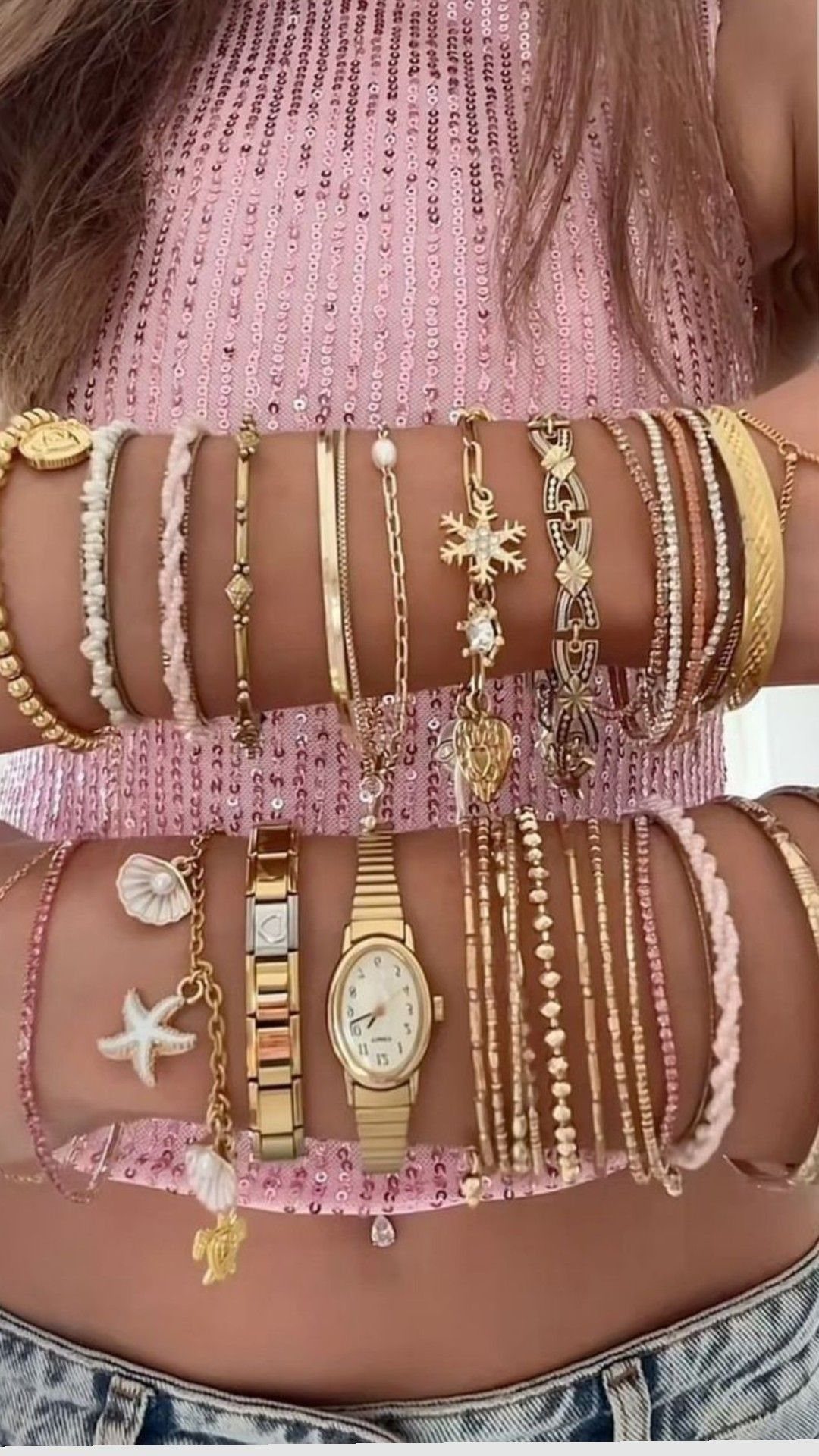 XOXO Jewelry Ideas: 10 Ways to Wear These Timeless Symbols 5 Gold chain and pearl bracelets layered on a person's wrist with a gold watch.